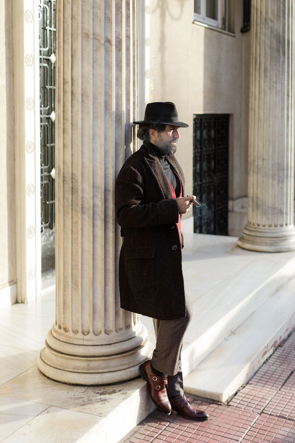 man and wearing coat, red vest and fedora hat smoking cigar street style